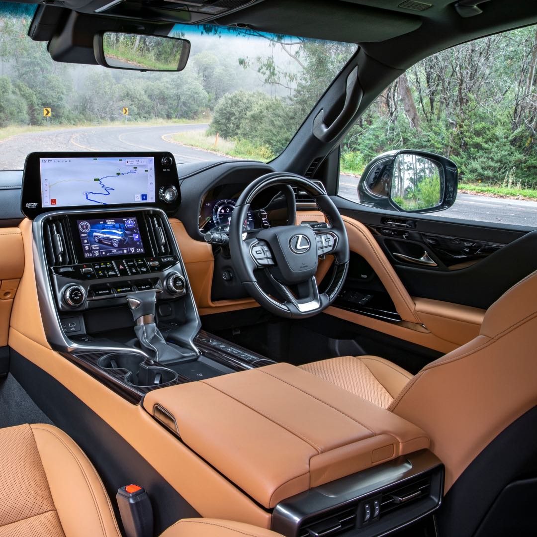 Interior of the 2022 LX - orange adorned leather and the lit up screens. The vehicle is sitting parked on the side of a windy road.
