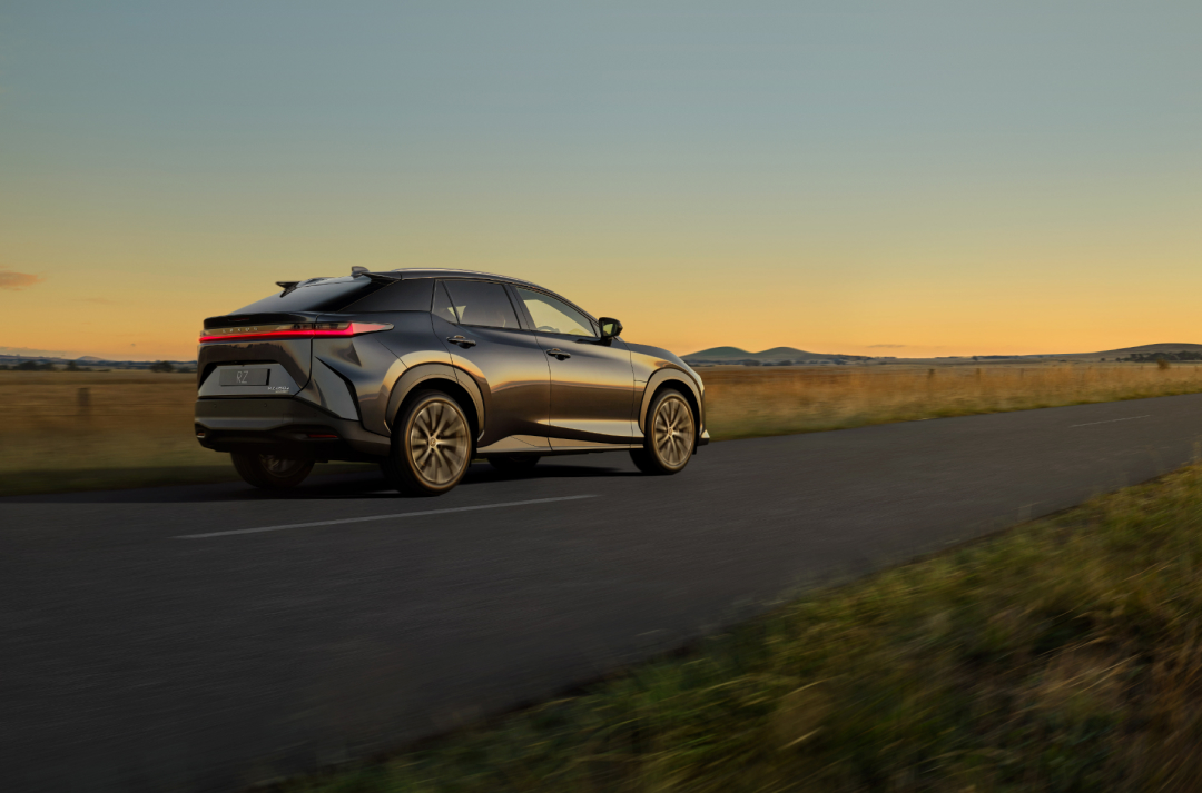 Rear side view of a Lexus RZ driving along an Australian country road as the sunsets.