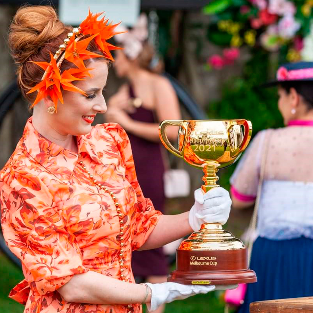 A woman wearing a red dress and headpiece holds the 2021 Cup.