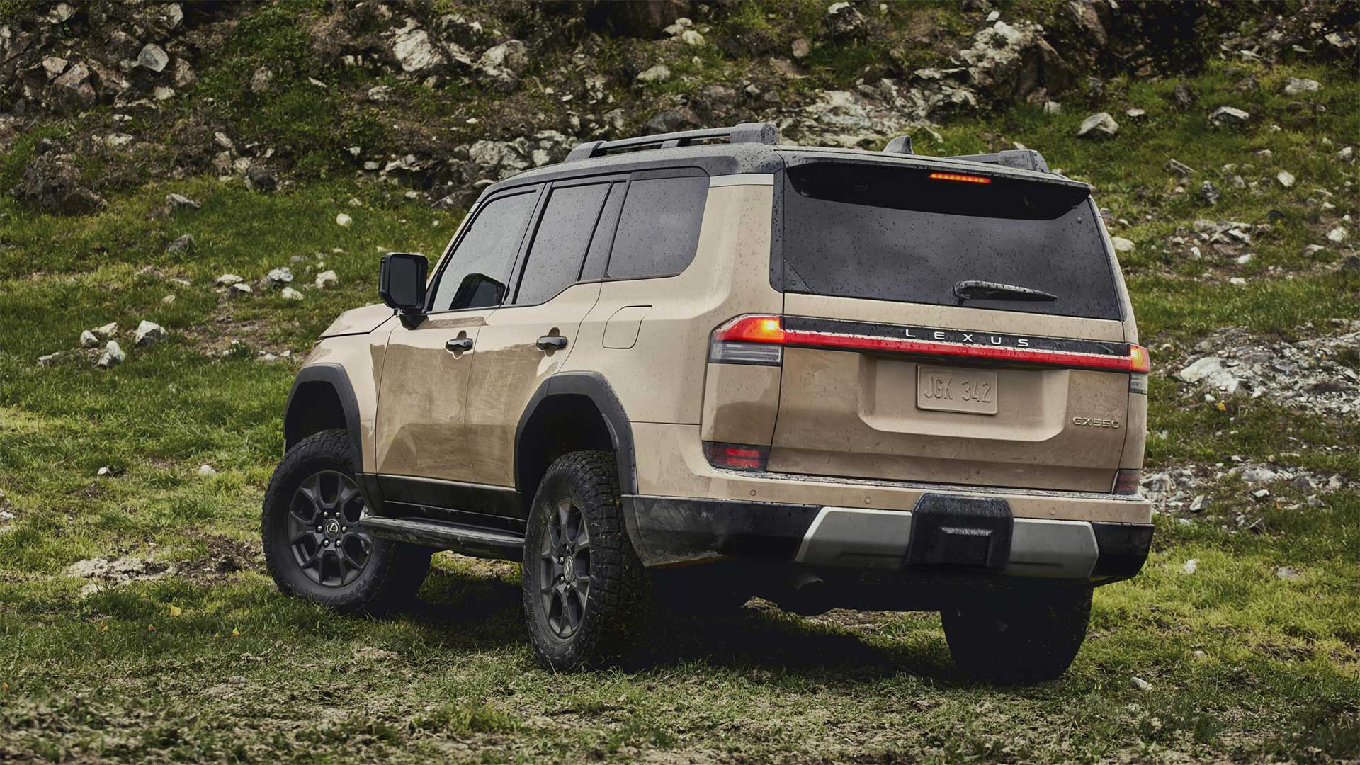 A Lexus GX is parked at the base of a green hill scattered with rocks and boulders