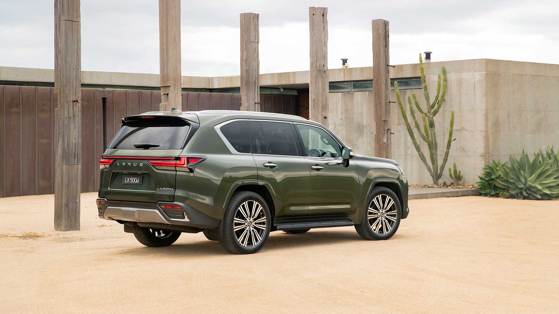 A green Lexus LX parked on a sandy driveway with wooden posts in the background and a cactus