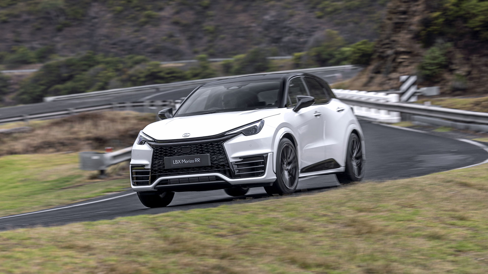 A white Lexus LBX Morizo RR driving along a winding road with trees in the background