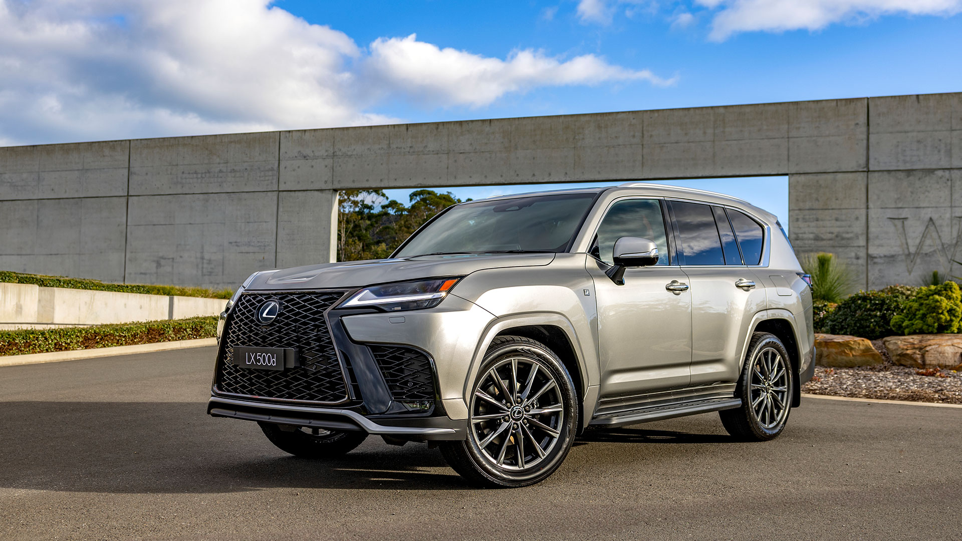 Metallic grey 2025 Lexus LX 500d F Sport parked in front of a modern concrete structure
